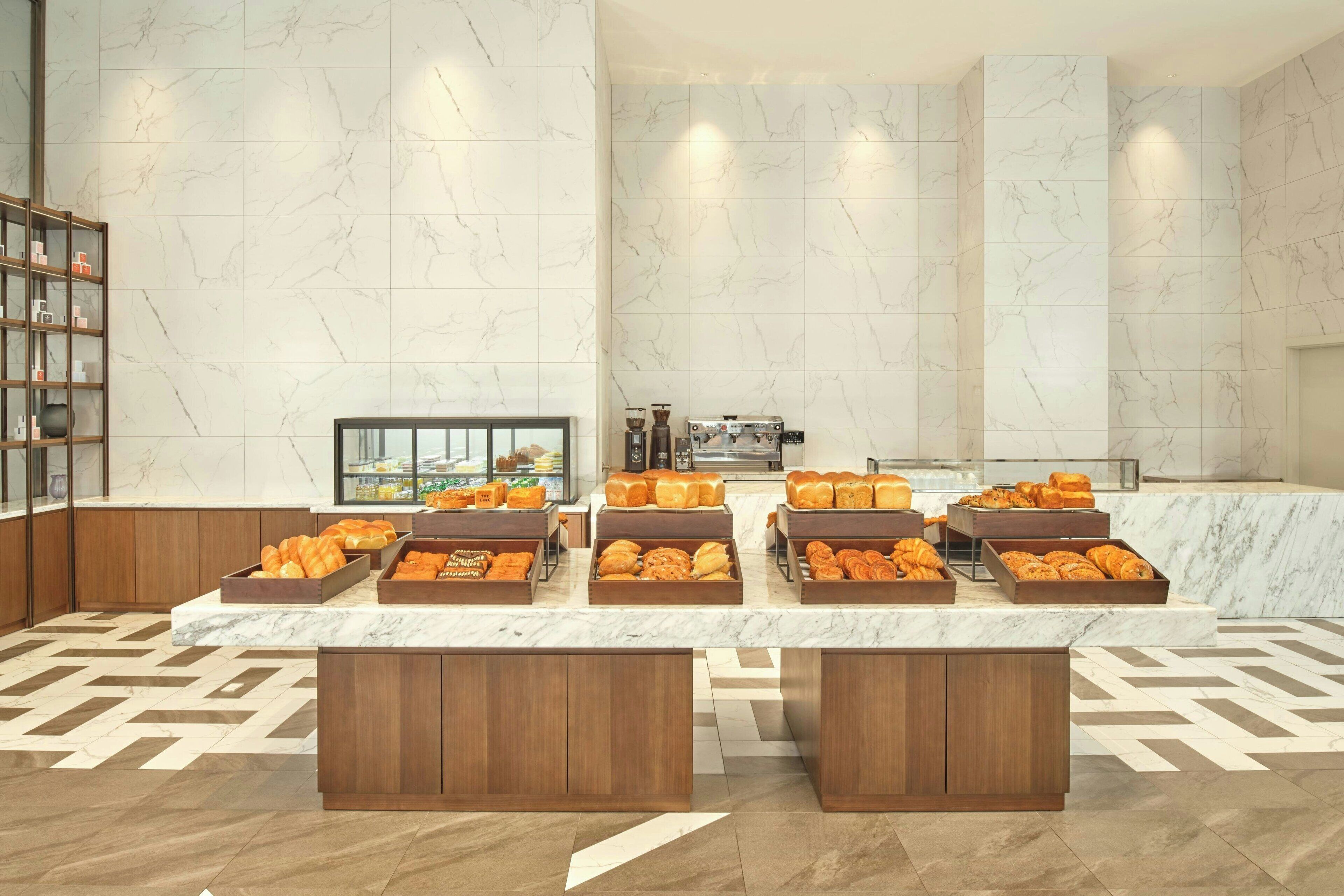 A breakfast buffet with various pastries and bread, marble walls, and wooden cabinets.