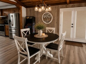 A dining area with a round table, white chairs, a vase with flowers, and a wall-mounted light fixture. - 8-Mile Lake Views/  Boathouse/  Fire Pit/  Pet Friendly (Frankston)