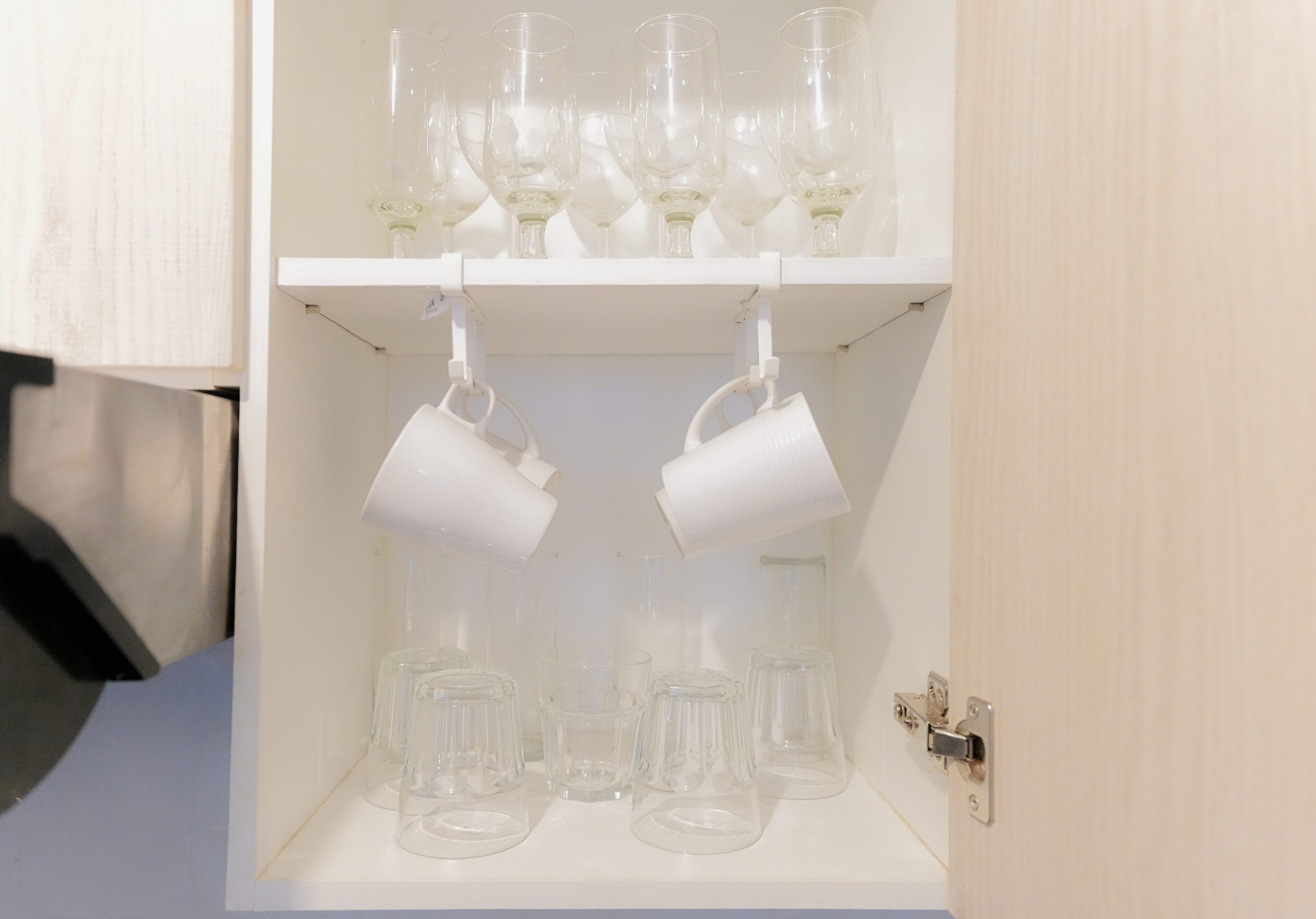 Un meuble blanc, doté d’étagères où sont rangés des verres à vin et des tasses.