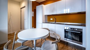 Une cuisine moderne avec des meubles blancs, un four encastré et une table de salle à manger ronde, accompagnée de chaises.