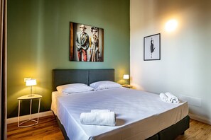 A neatly made bed with white linens and a rolled towel, two bedside lamps, a framed painting of a couple, and a wall-mounted light fixture. - YiD Romito 3bdr design apartment (Firenze)