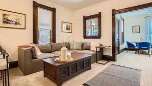 Una sala de estar con un sofá modular, una mesa de centro y una mesita auxiliar. Hay cuadros enmarcados en las paredes y una ventana con vistas.