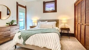 Un dormitorio con cama, mesitas de noche, cómoda, espejo y ventana.