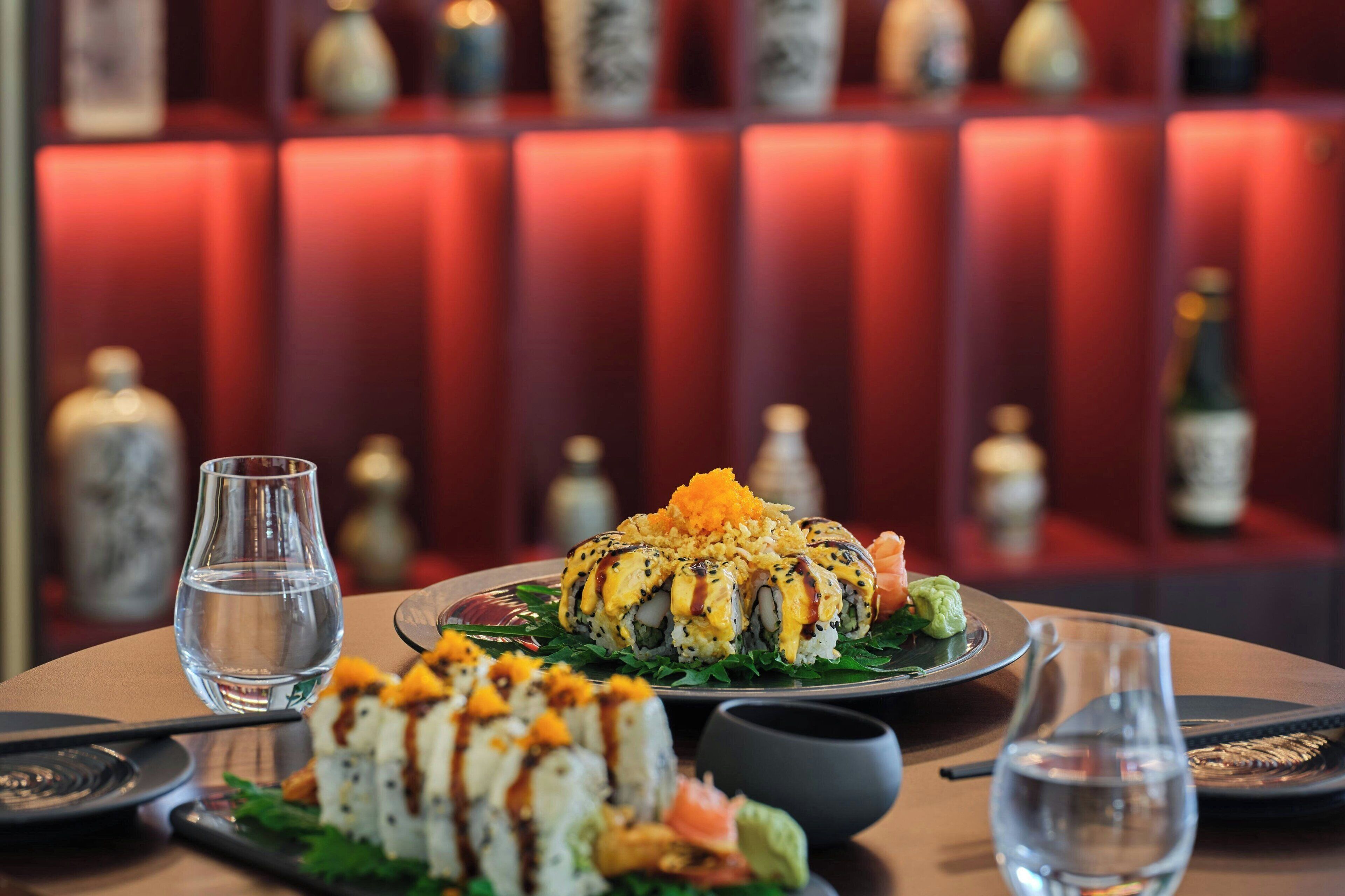 A sushi dish on a plate with chopsticks and a glass of water on a table.