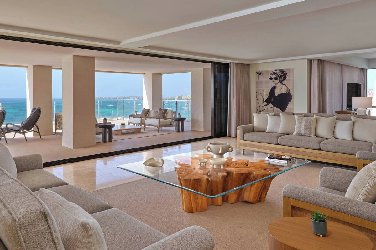 Een ruime woonkamer met een grote glazen salontafel, zachte zitplaatsen en uitzicht op zee.