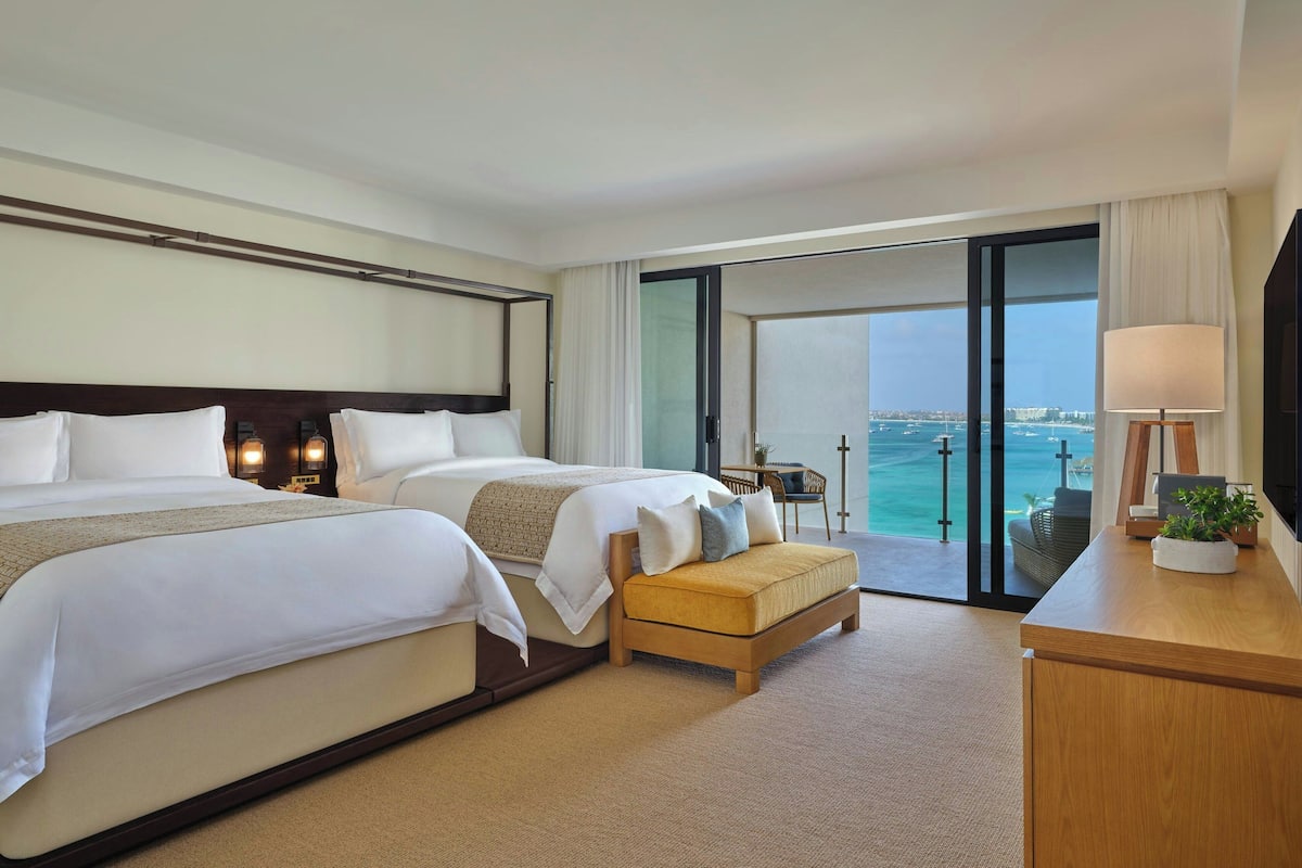 Een hotelkamer met twee bedden, een bank, een bureau en uitzicht op zee.