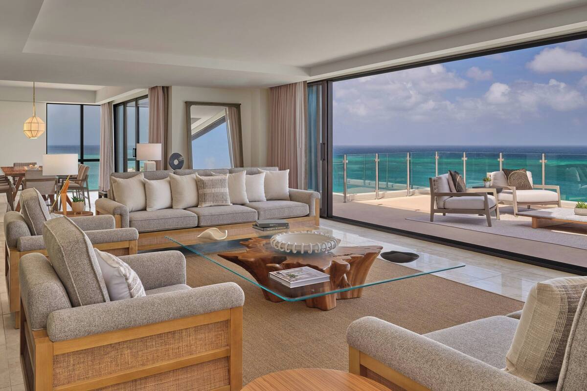 Een moderne hotelkamer met een ruim balkon, een zithoek, een glazen salontafel en uitzicht op de oceaan.