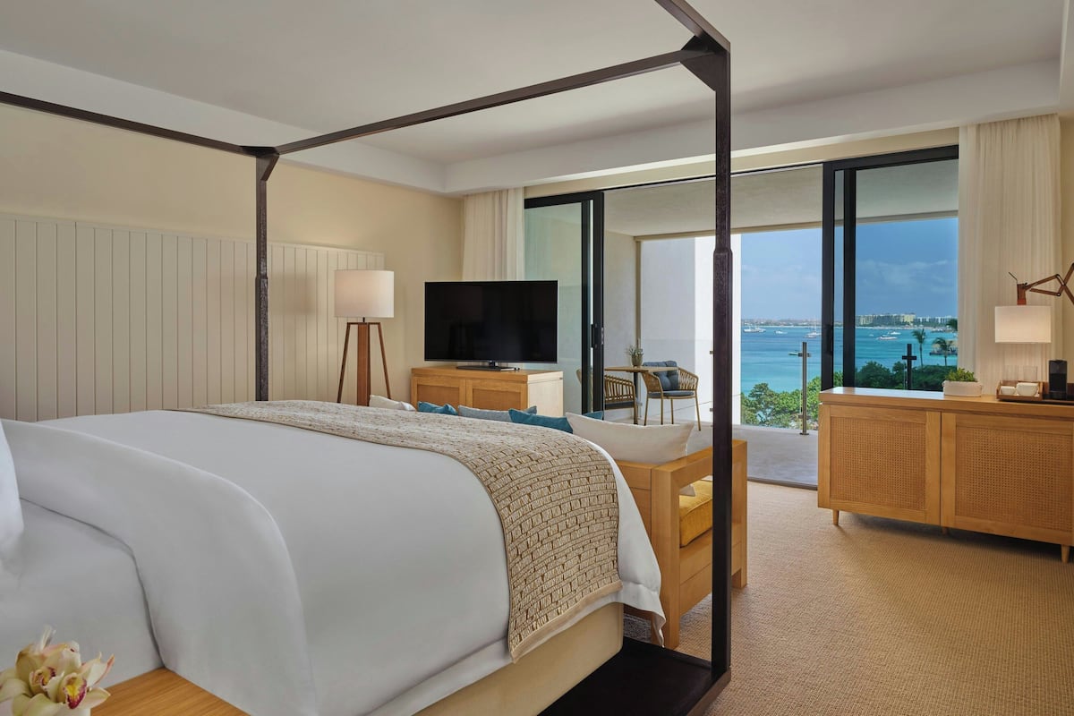 Hotelkamer met een hemelbed, een flatscreen televisie, een houten bureau en uitzicht op zee.