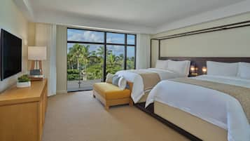 Habitación de hotel con dos camas, televisión, escritorio con lámpara y vistas a palmeras.