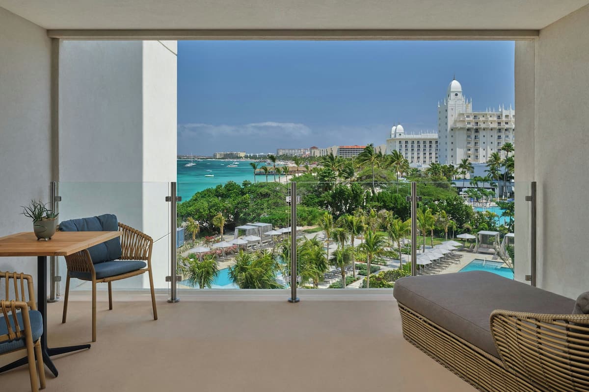 Een balkon met uitzicht op een resort zwembad, palmbomen en een gebouw in de verte.