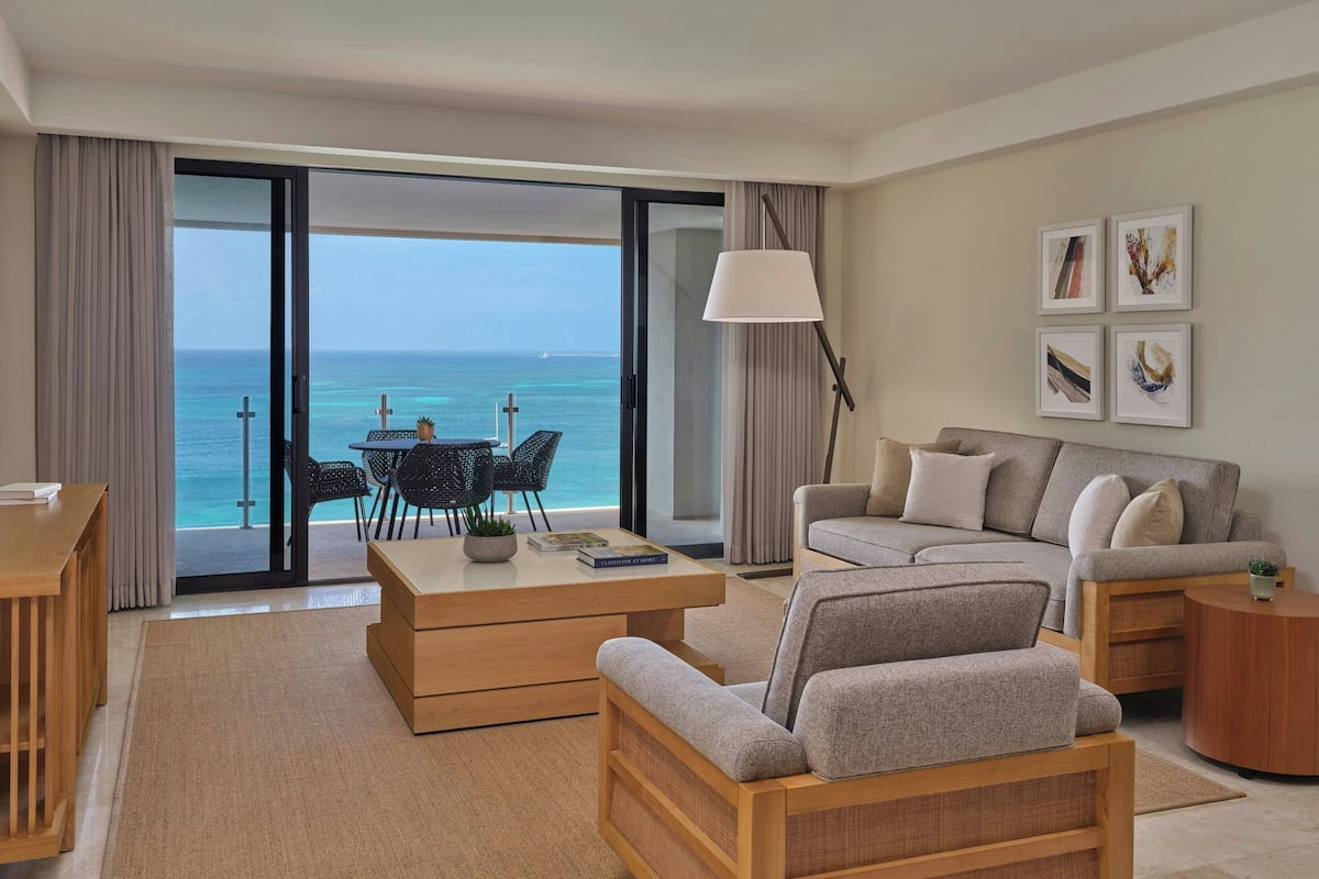 Een moderne woonkamer met uitzicht op zee, een bank, een salontafel en een eethoek met stoelen.