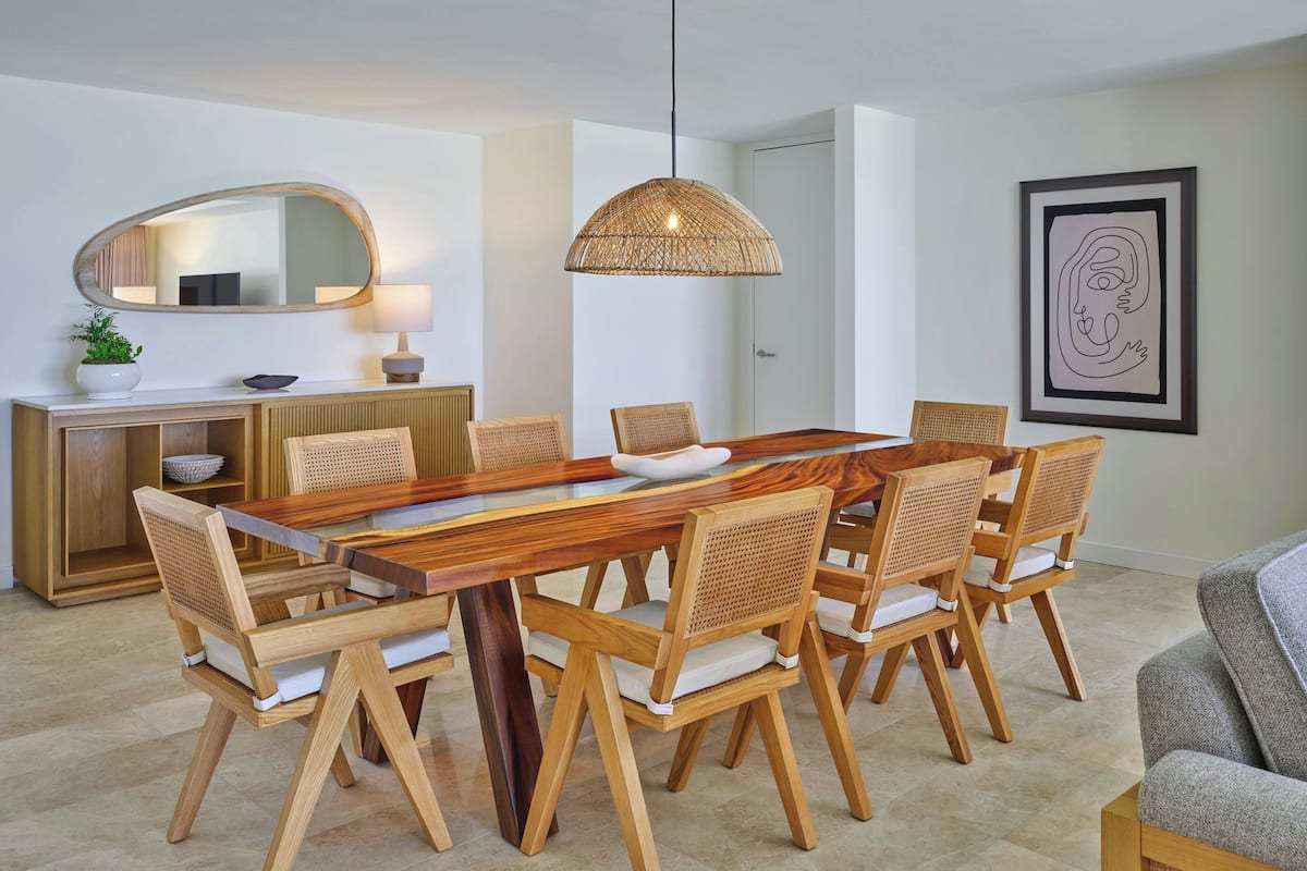 Een eetruimte met een houten tafel en stoelen, een hanglamp, een spiegel, en een lijst met kunstwerk aan de muur.