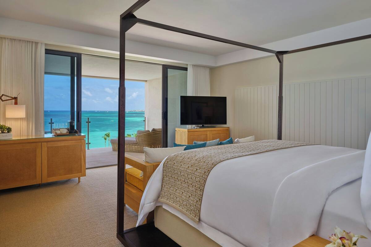 Een moderne hotelkamer met een groot bed, een televisie, een houten dressoir en uitzicht op de oceaan.