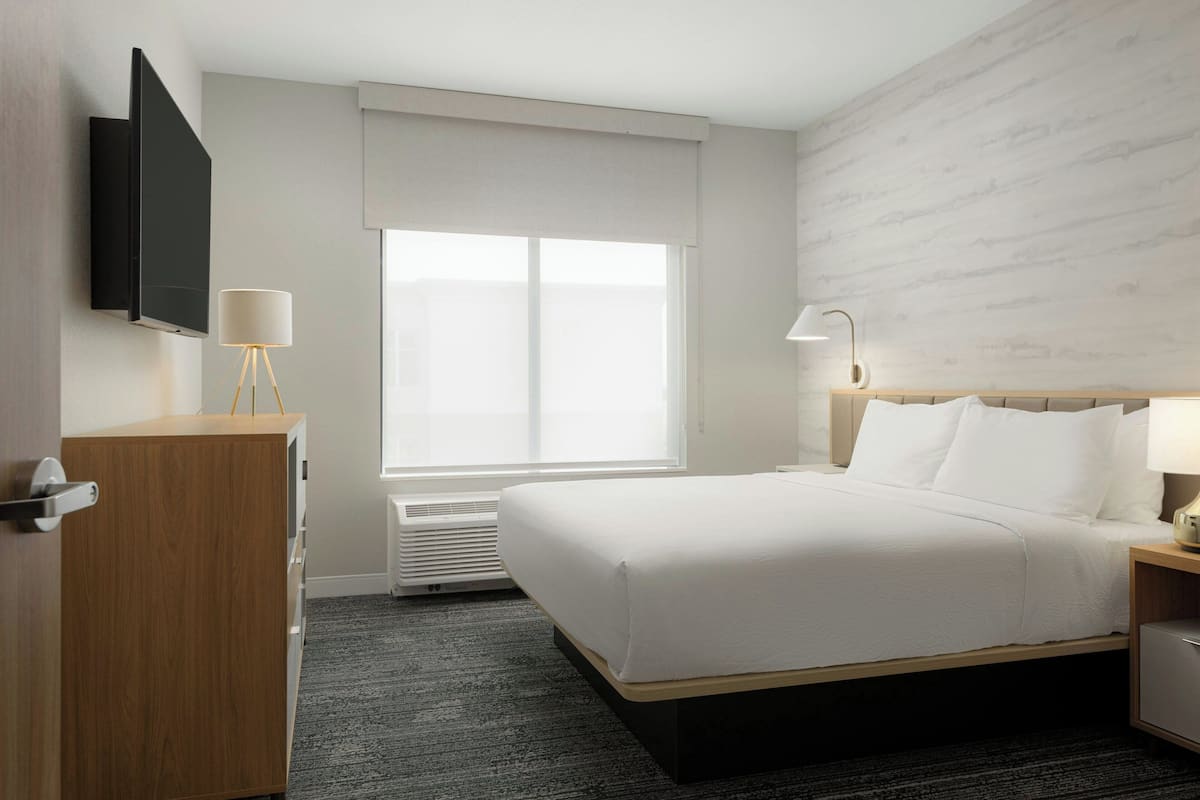 Een hotelkamer met een bed, nachtkastje, lamp en een flatscreen televisie aan de muur.