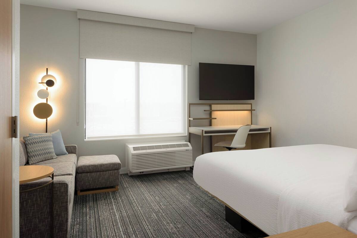 Een moderne hotelkamer met een bed, een bureau, een stoel, een bank, een televisie en een wandlamp.