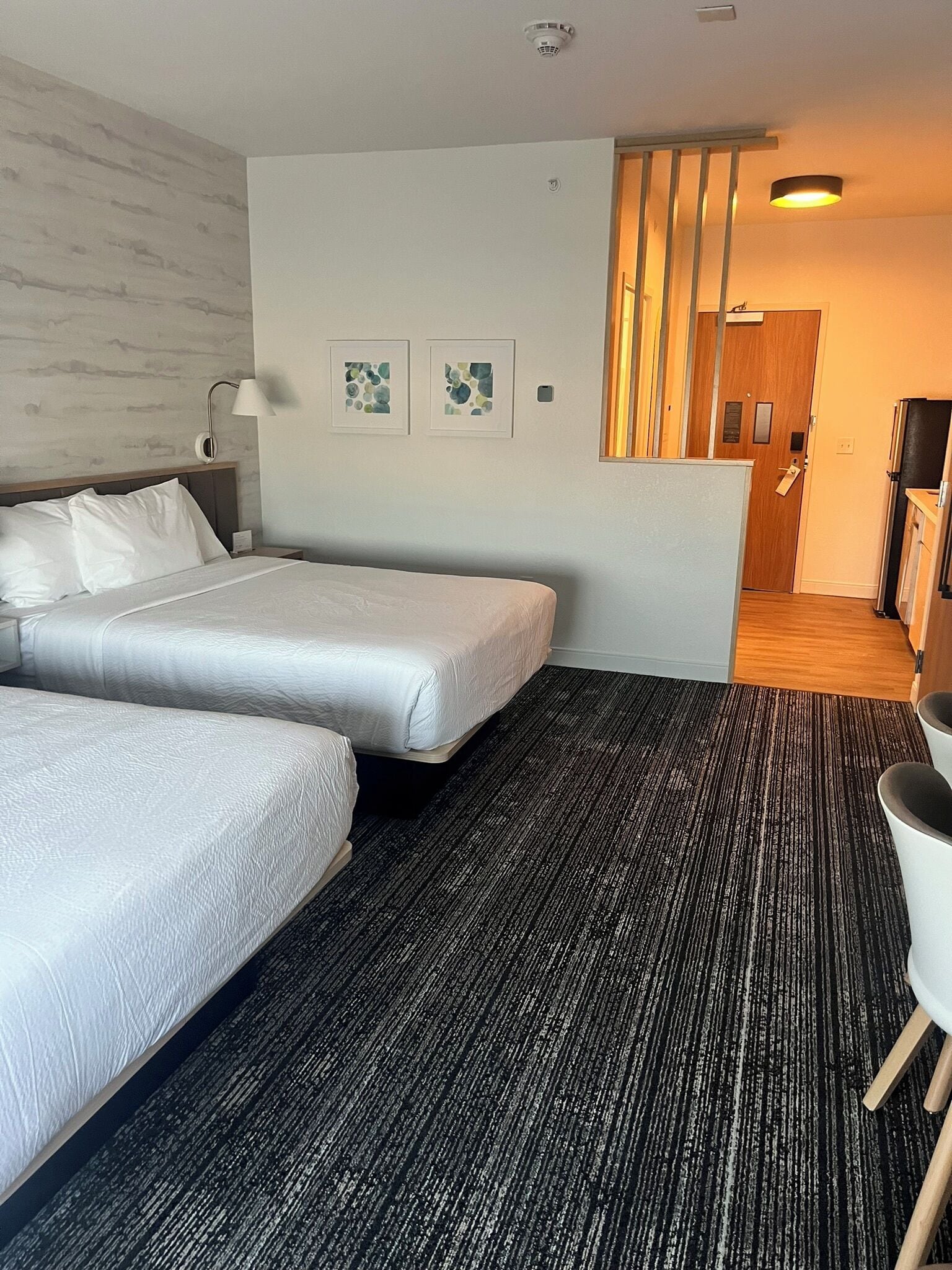 Ein Hotelzimmer mit zwei Betten, einem Schreibtisch, einem Stuhl und einer kleinen Küchenzeile.
