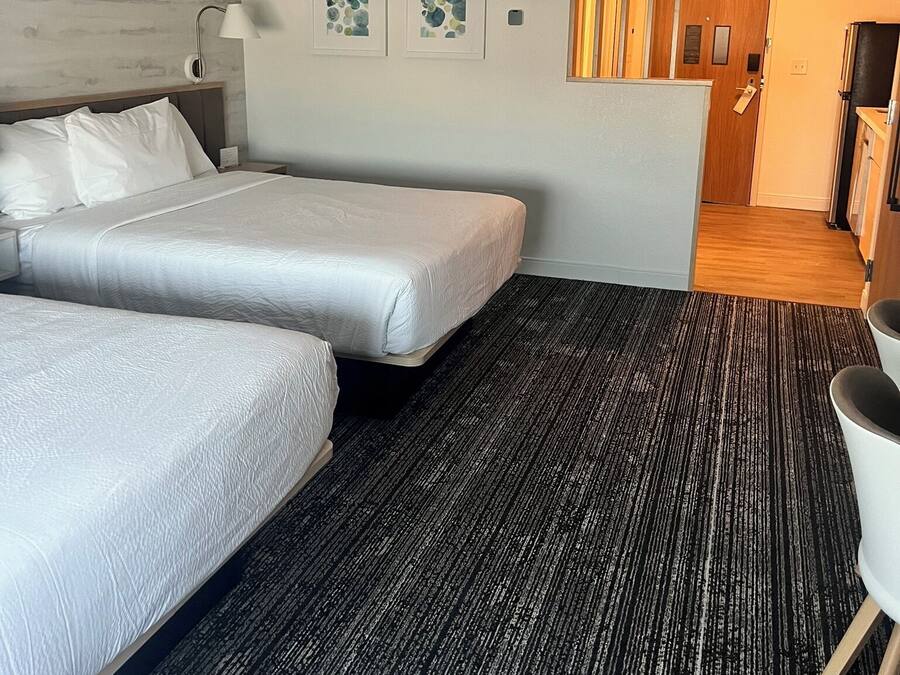 Ein Hotelzimmer mit zwei Betten, einem Schreibtisch, einem Stuhl und einer kleinen Küchenzeile.