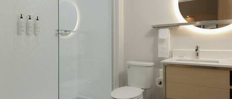 Un baño moderno con cabina de ducha de vidrio, inodoro y tocador con espejo.