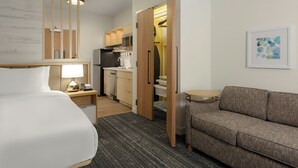 Una habitación de hotel con cama, sofá, escritorio con lámpara, kitchenette y una pequeña mesa de comedor.