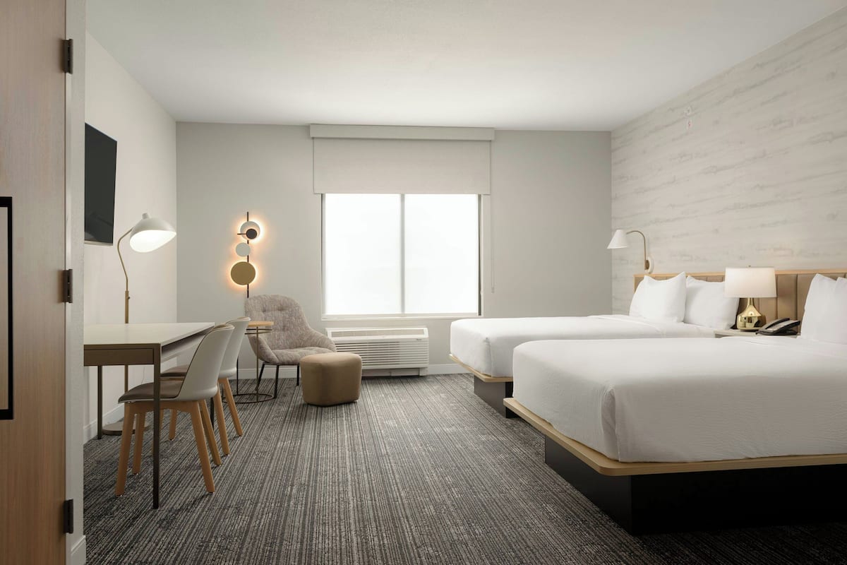 Een hotelkamer met twee bedden, een bureau, een stoel, een lamp en een groot raam.