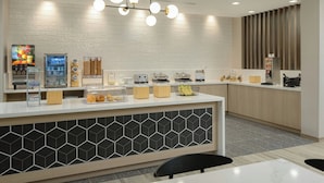 Un área de cocina moderna con encimera blanca, cafetera, exposición de frutas y lámpara colgante.