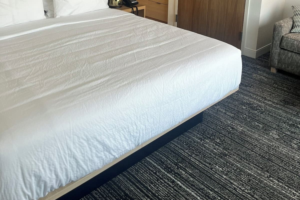 Een hotelkamer met een groot bed, een houten garderobe, een kitchenette en een grijze fauteuil.