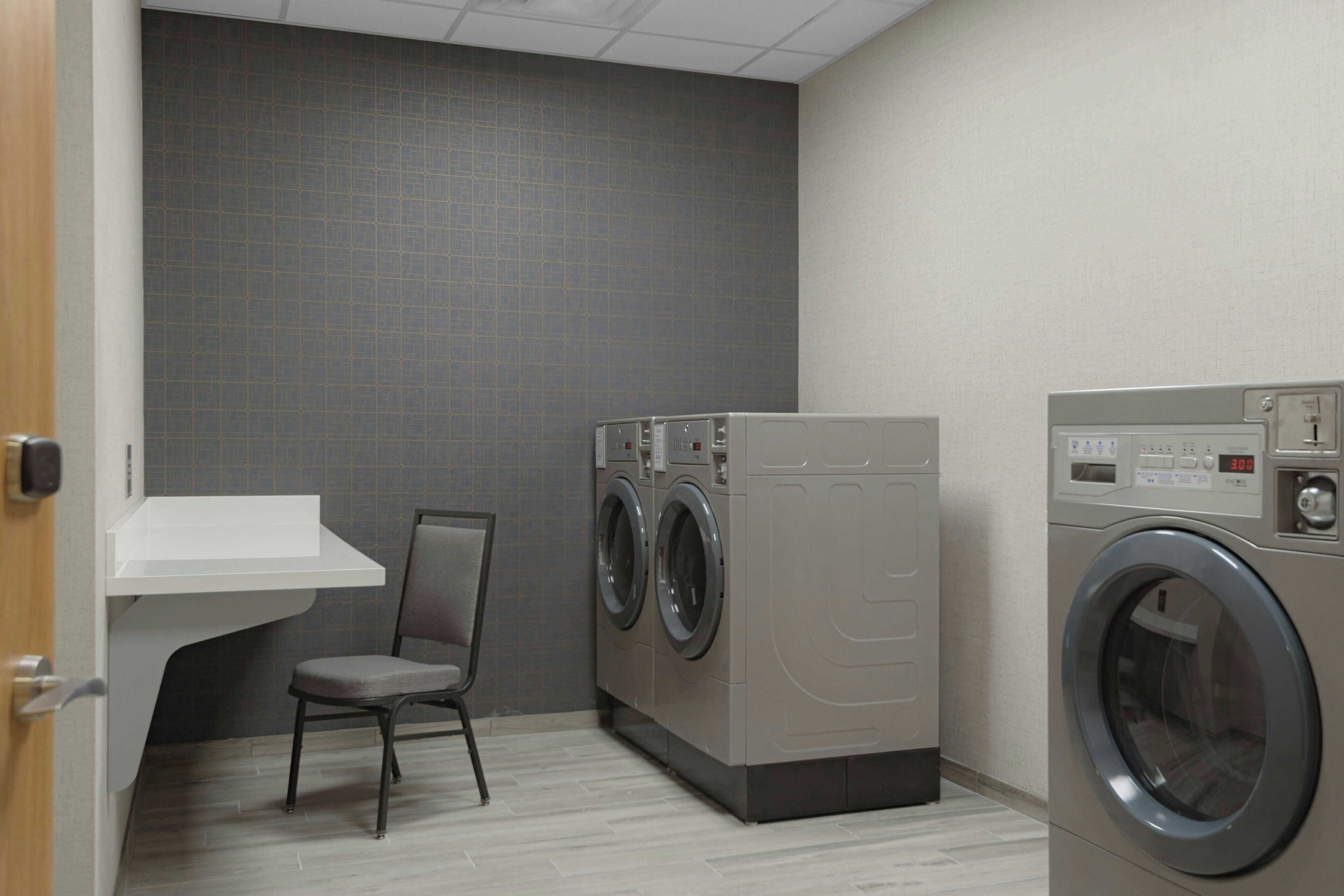 A laundry room with two washing machines, a chair, and a white sink.