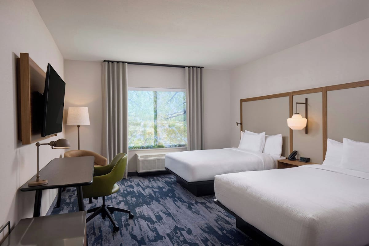 Une chambre d’hôtel avec deux lits, un bureau, une chaise, une télévision et une fenêtre avec des rideaux.