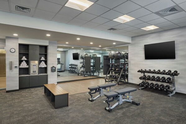 Un gimnasio moderno con equipo de levantamiento de pesas, bancos y un espejo grande.