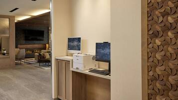 A reception area with a modern design, featuring a reception desk, two monitors, a printer, and a fireplace in the background.