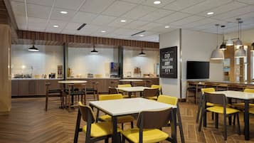 A modern restaurant with wooden flooring, yellow chairs, and white tables.