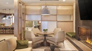 Ein modernes Wohnzimmer mit rundem Tisch, zwei Sesseln, einer Couch, einem Kamin und einem an der Wand montierten Fernseher.
