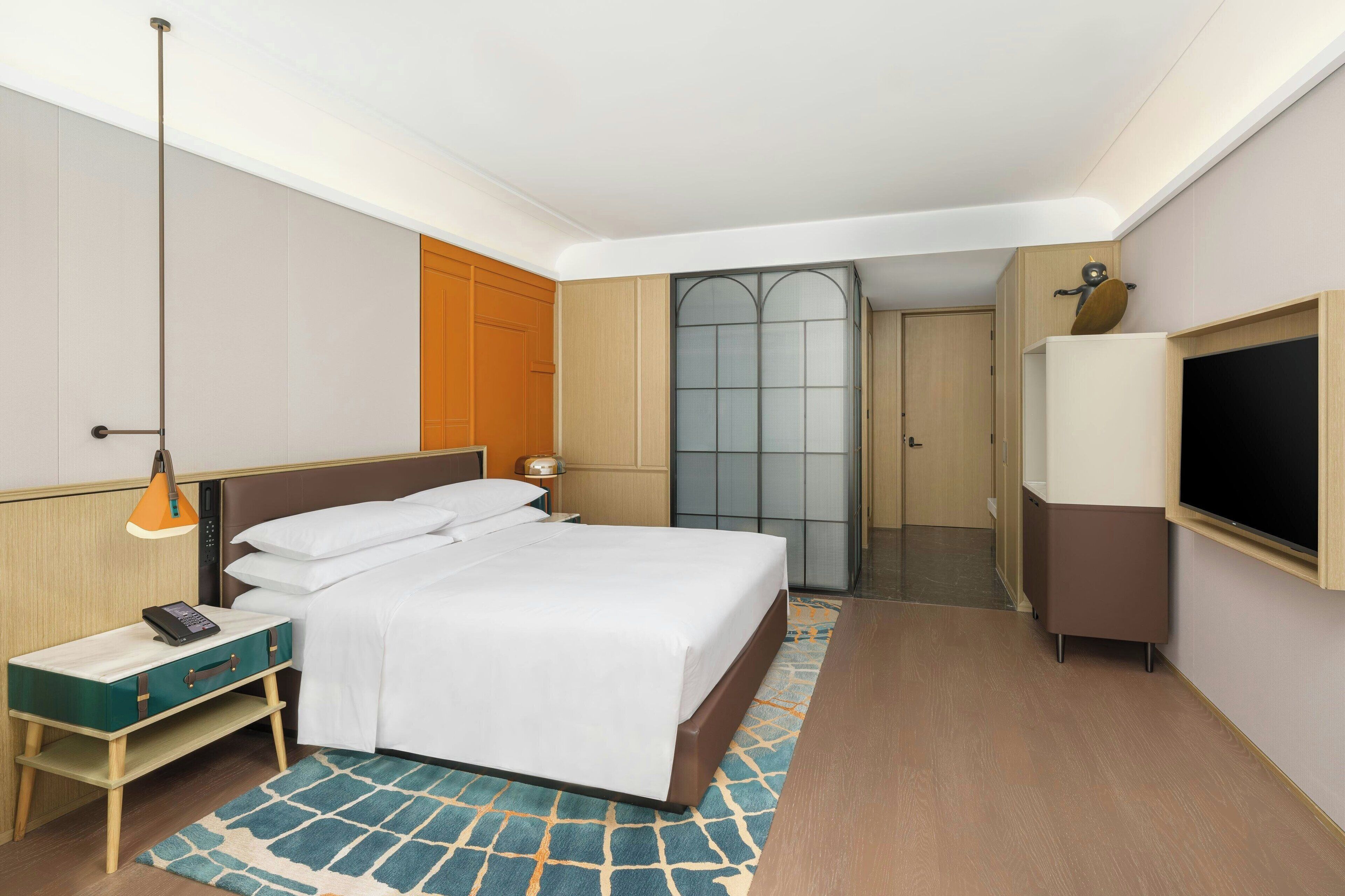 A hotel room with a bed, bedside table, lamp, TV, and a wardrobe.