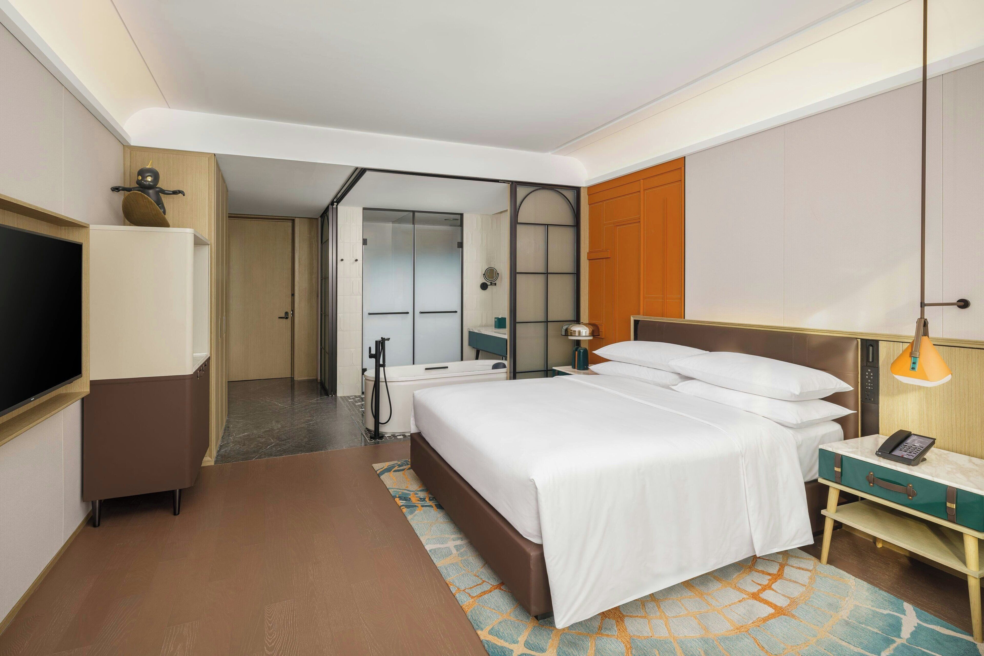 A hotel room with a bed, bedside table, lamp, and a television.
