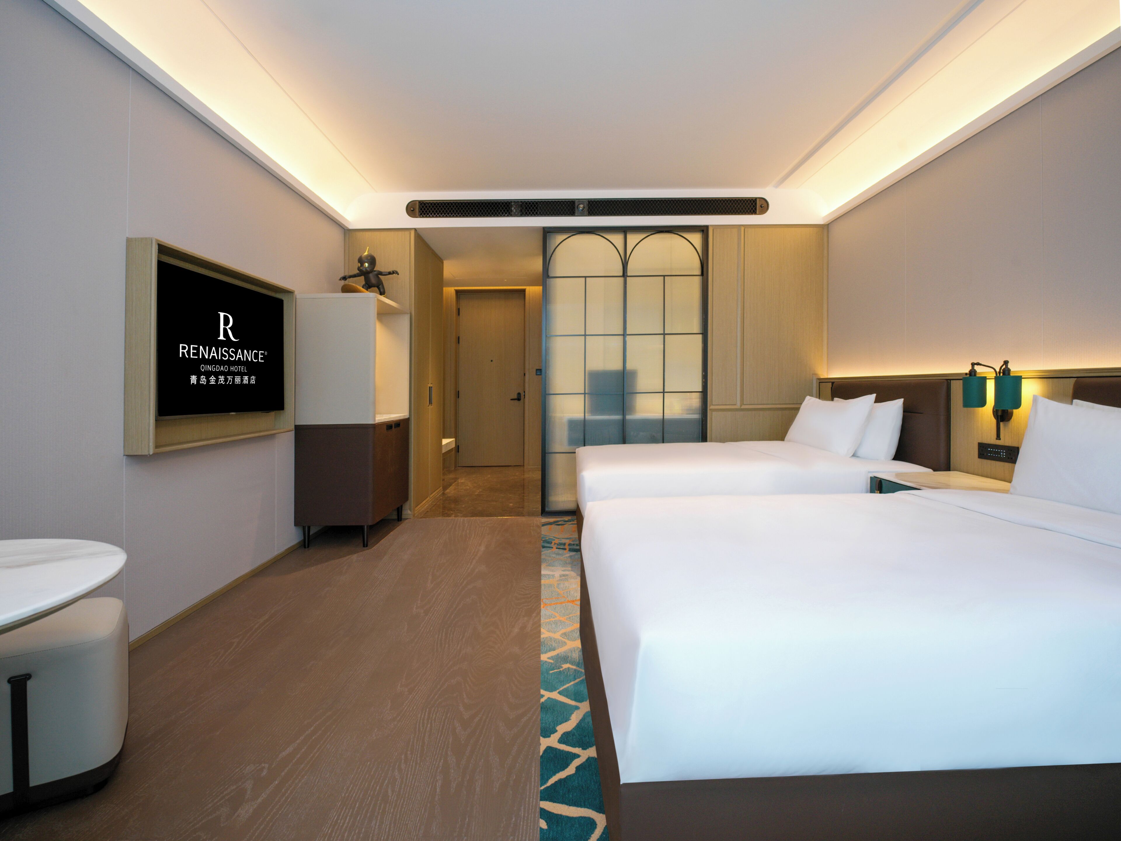 A hotel room with two beds, a desk, a chair, a TV, and a minibar.