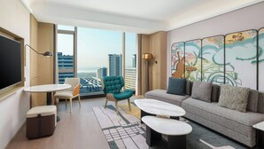 Une chambre d’hôtel moderne dotée d’une grande fenêtre donnant sur la ville, d’un canapé, d’une petite table, d’une chaise et d’un élément décoratif mural.