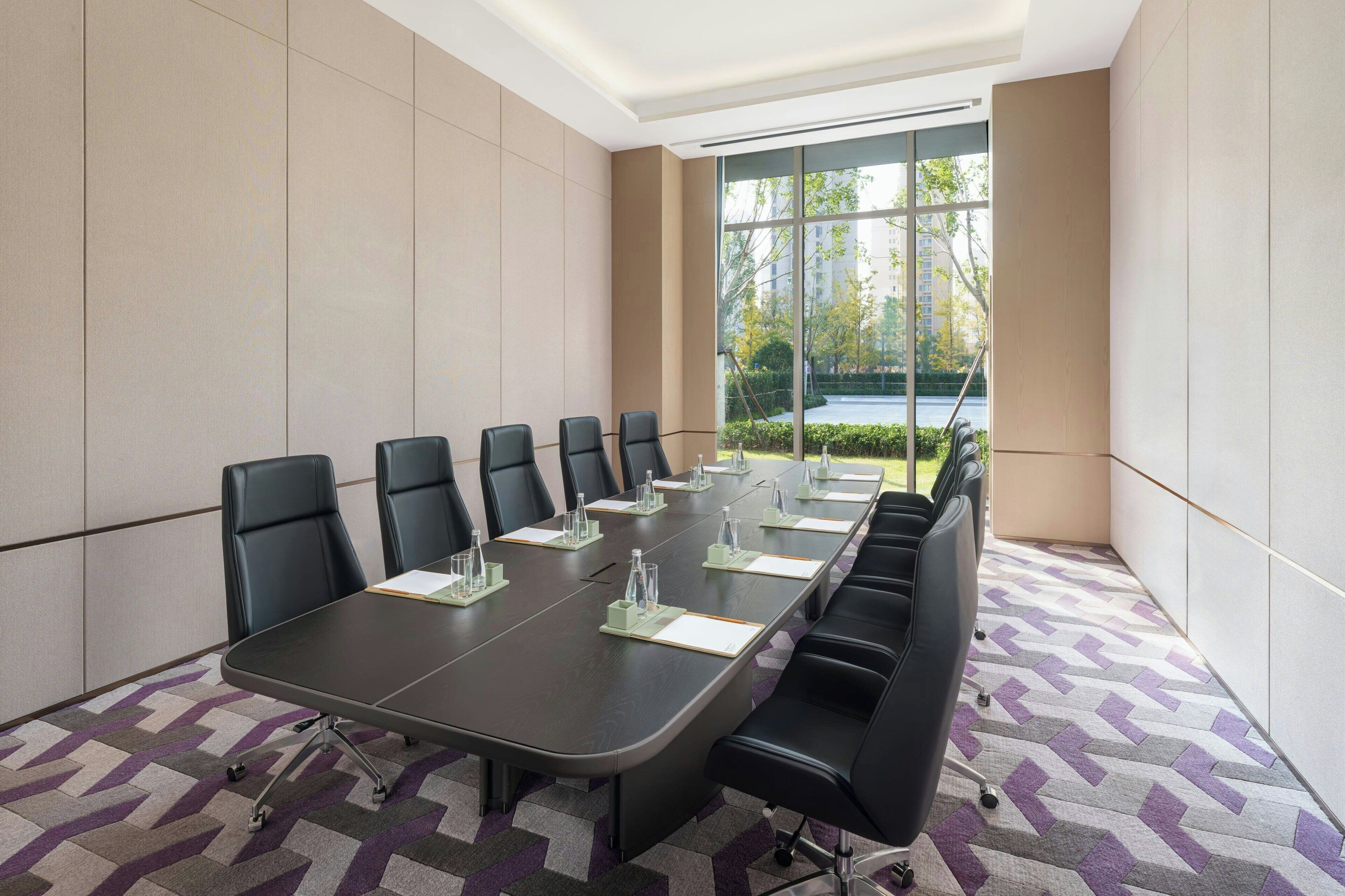 A conference room with a long table, black chairs, and a patterned carpet.