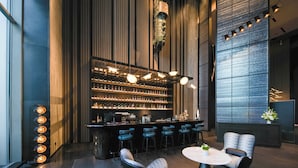 Un espace bar moderne, avec un long comptoir rempli de bouteilles, des tabourets de bar et une table ronde entourée de chaises.