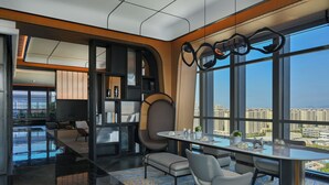 Une chambre d’hôtel moderne dotée d’une grande fenêtre donnant sur la ville, d’un coin repas avec une table et des chaises, et d’une bibliothèque.