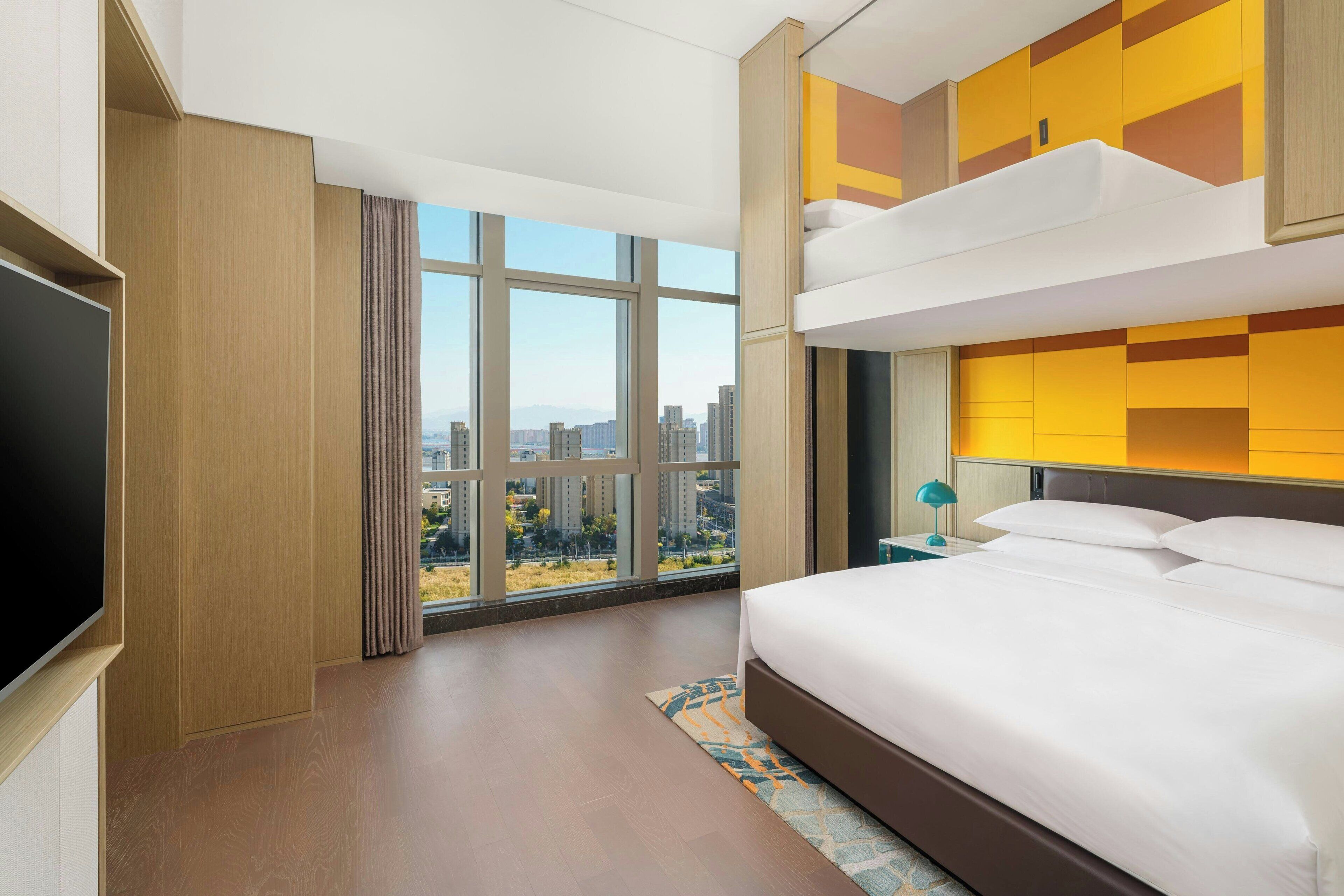 Een hotelkamer met een groot bed, een televisie en uitzicht op een stadsgezicht door grote ramen.