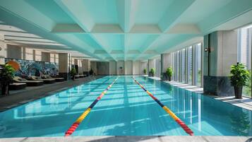 Una piscina interior larga con separadores de carril, sillas de descanso y plantas en macetas a lo largo de los lados.