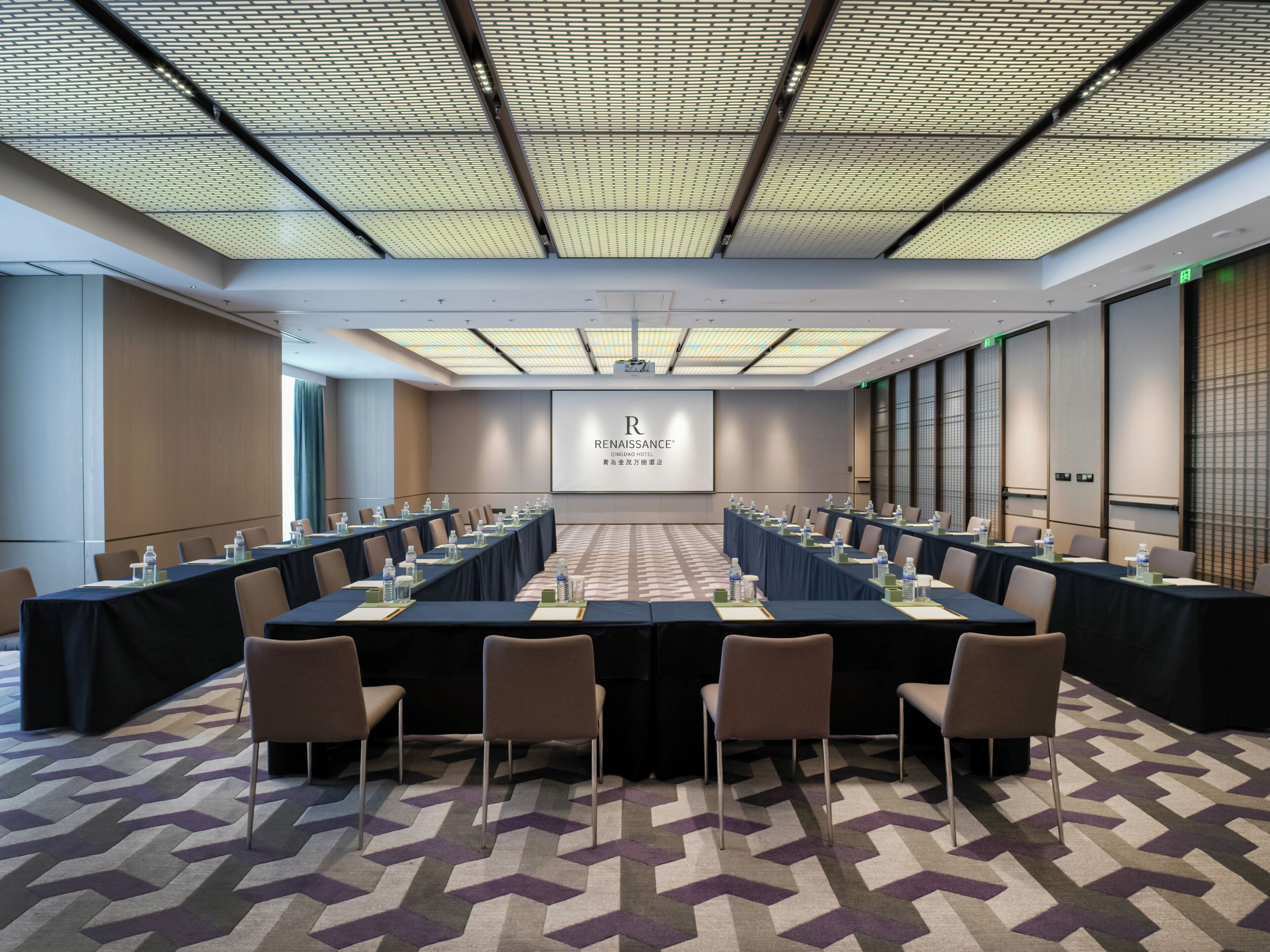 A conference room with a long table, chairs, and a presentation screen.