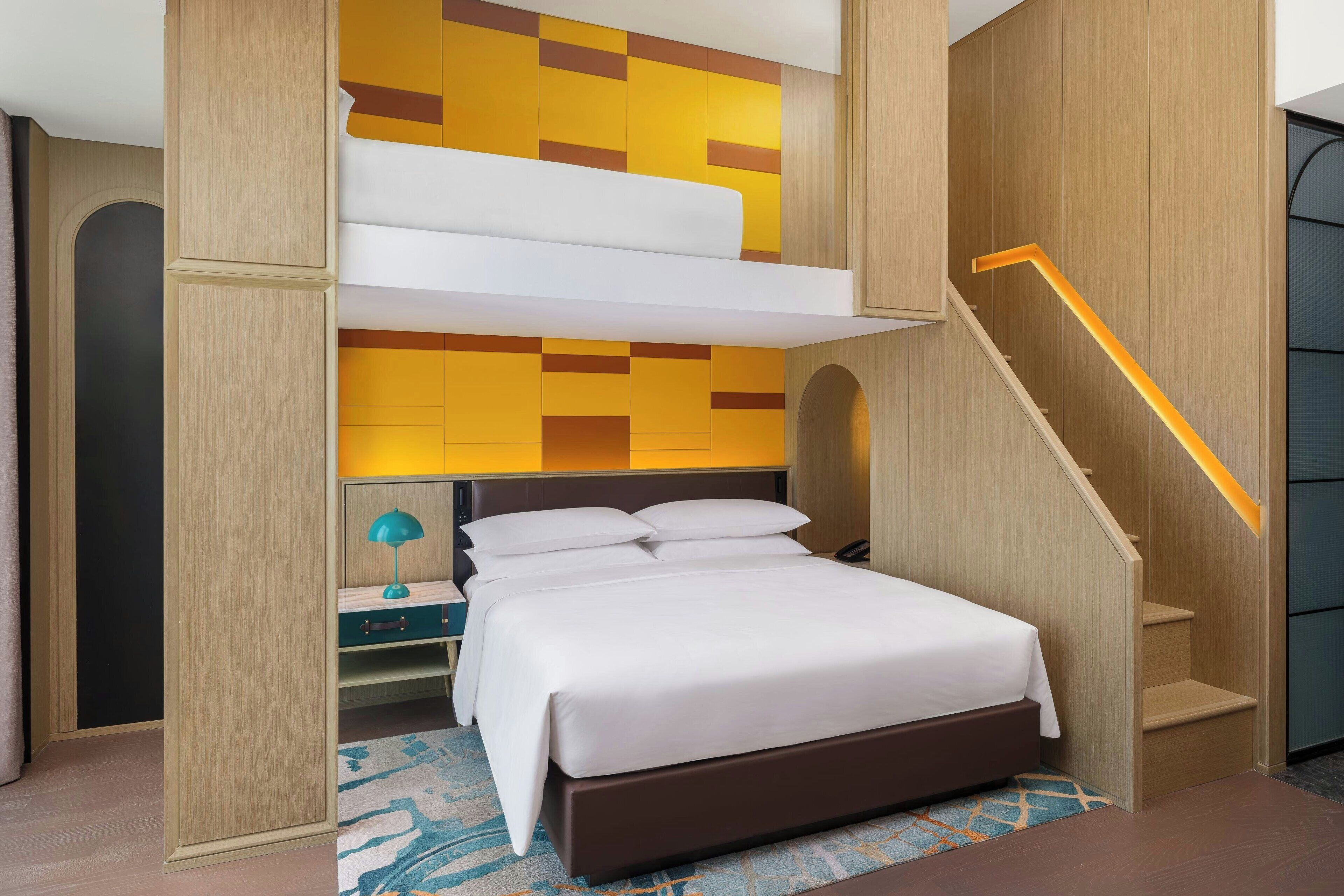 Een moderne hotelkamer met een bed, ingebouwde opbergruimte, een bureau met lamp en een trap met verlichte leuning.