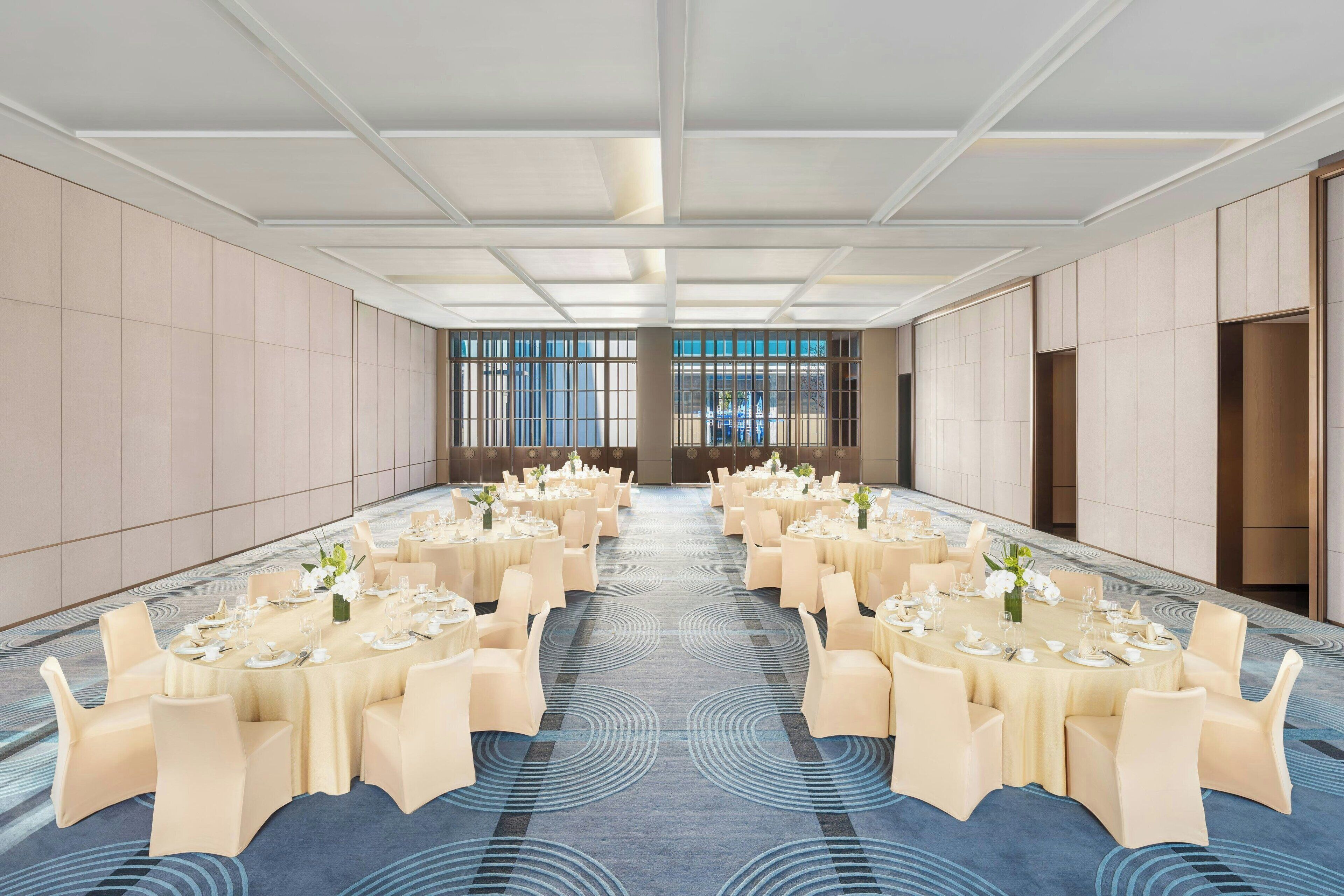A spacious conference room with round tables and chairs, a patterned carpet, and a modern ceiling design.