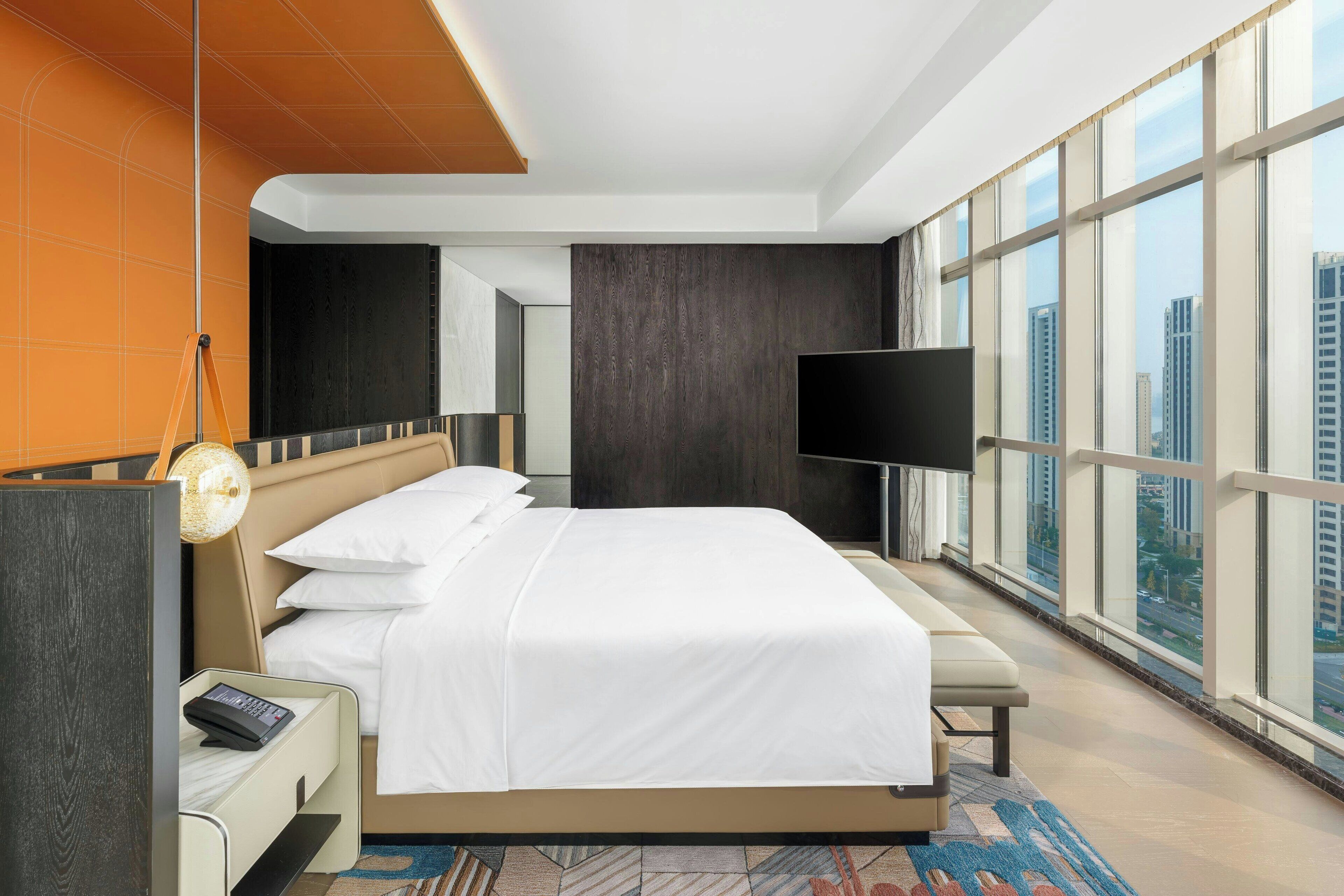 Una camera d'albergo moderna con un letto grande, una televisione a schermo piatto e vista sulla città da ampie finestre.