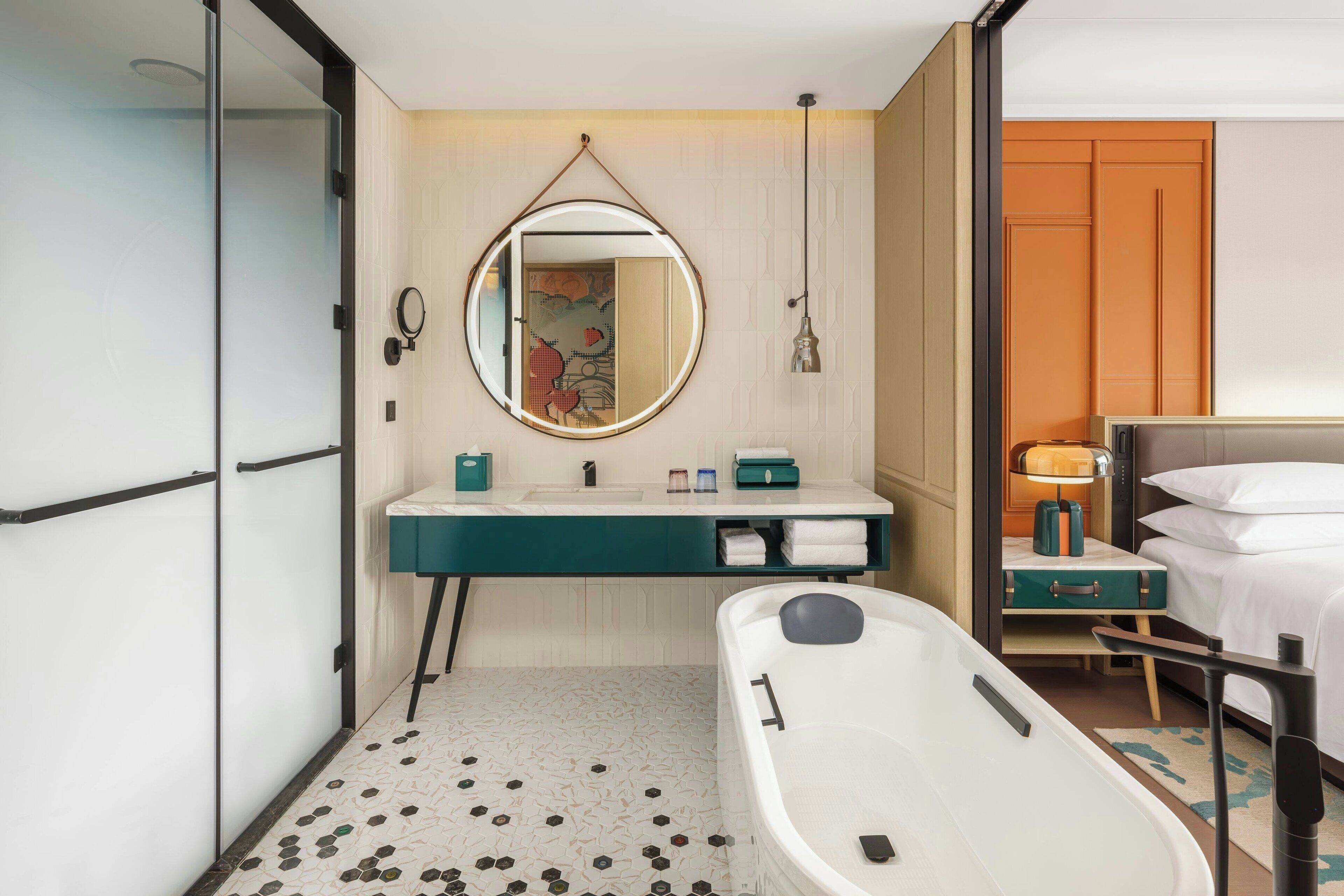 A modern bathroom with a freestanding bathtub, a round mirror, a sink with a green countertop, and a wooden cabinet.