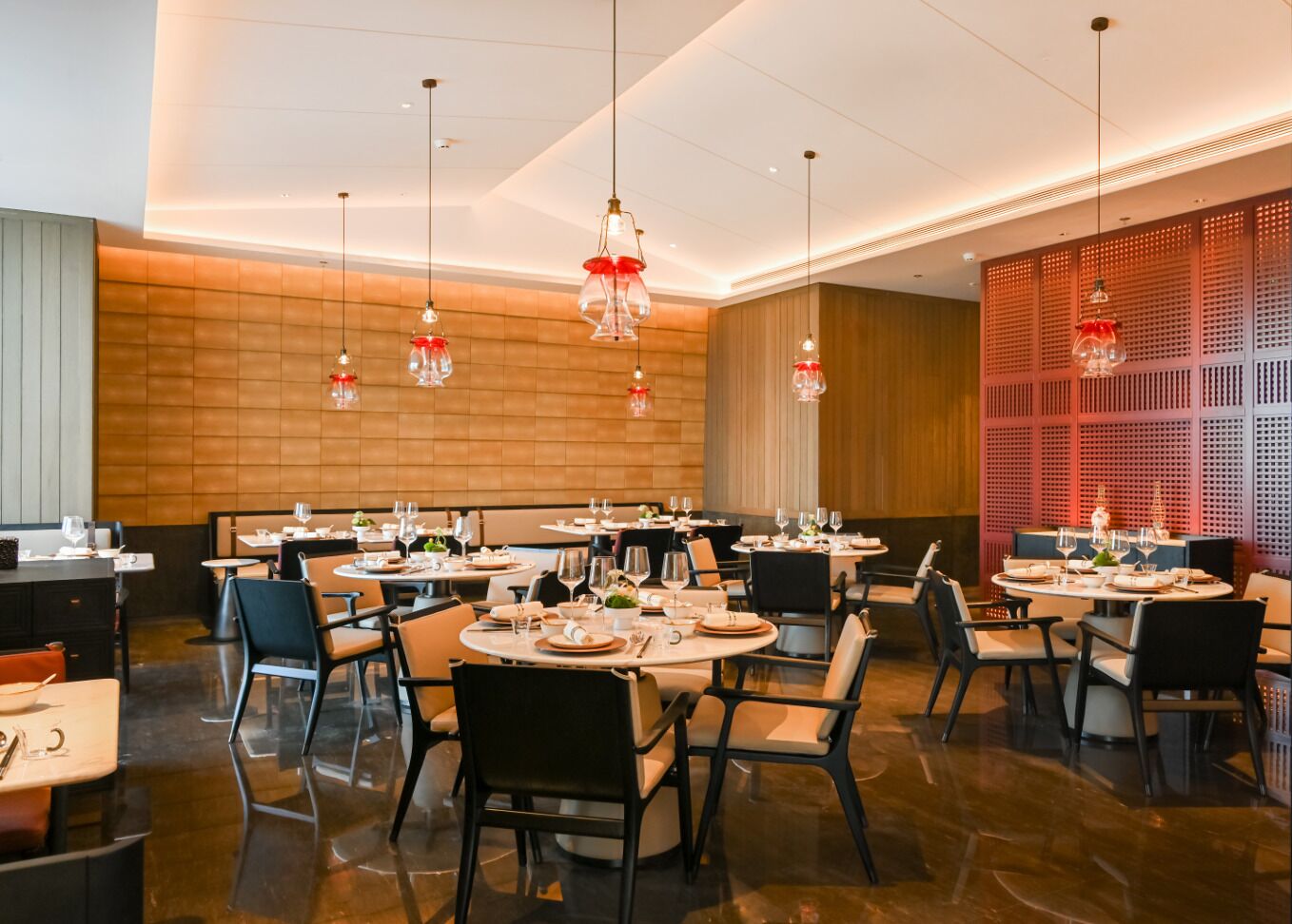 Un restaurant moderne avec des tables rondes et des chaises noires, agrémenté d’un mur en bois et de lumières décoratives rouges.