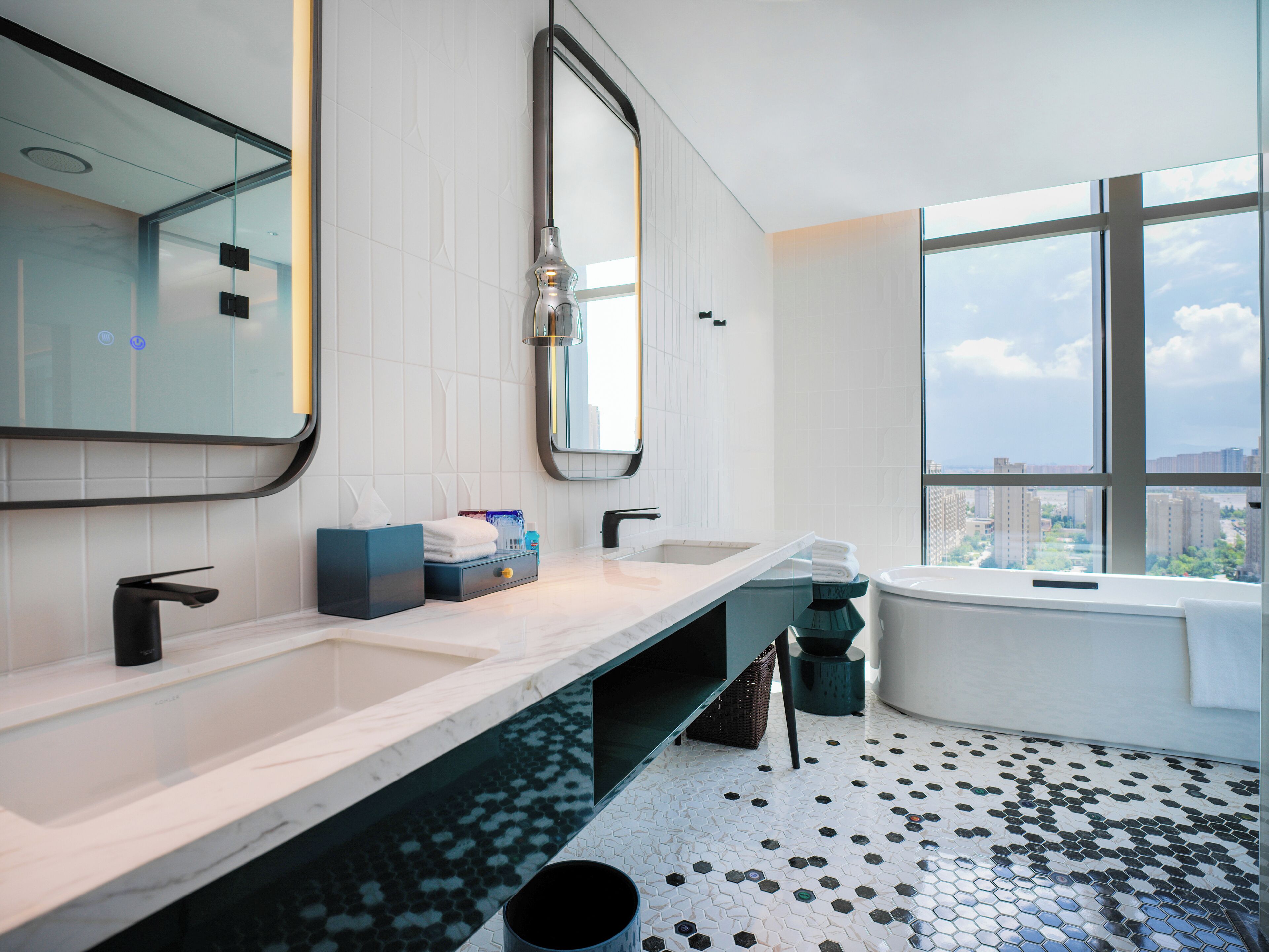 A modern bathroom with a large mirror, two sinks, a bathtub, and a view of the city through large windows.