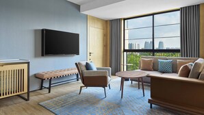 A modern living room with a large window, a flat-screen TV mounted on the wall, a sofa, a bench, and a small table.