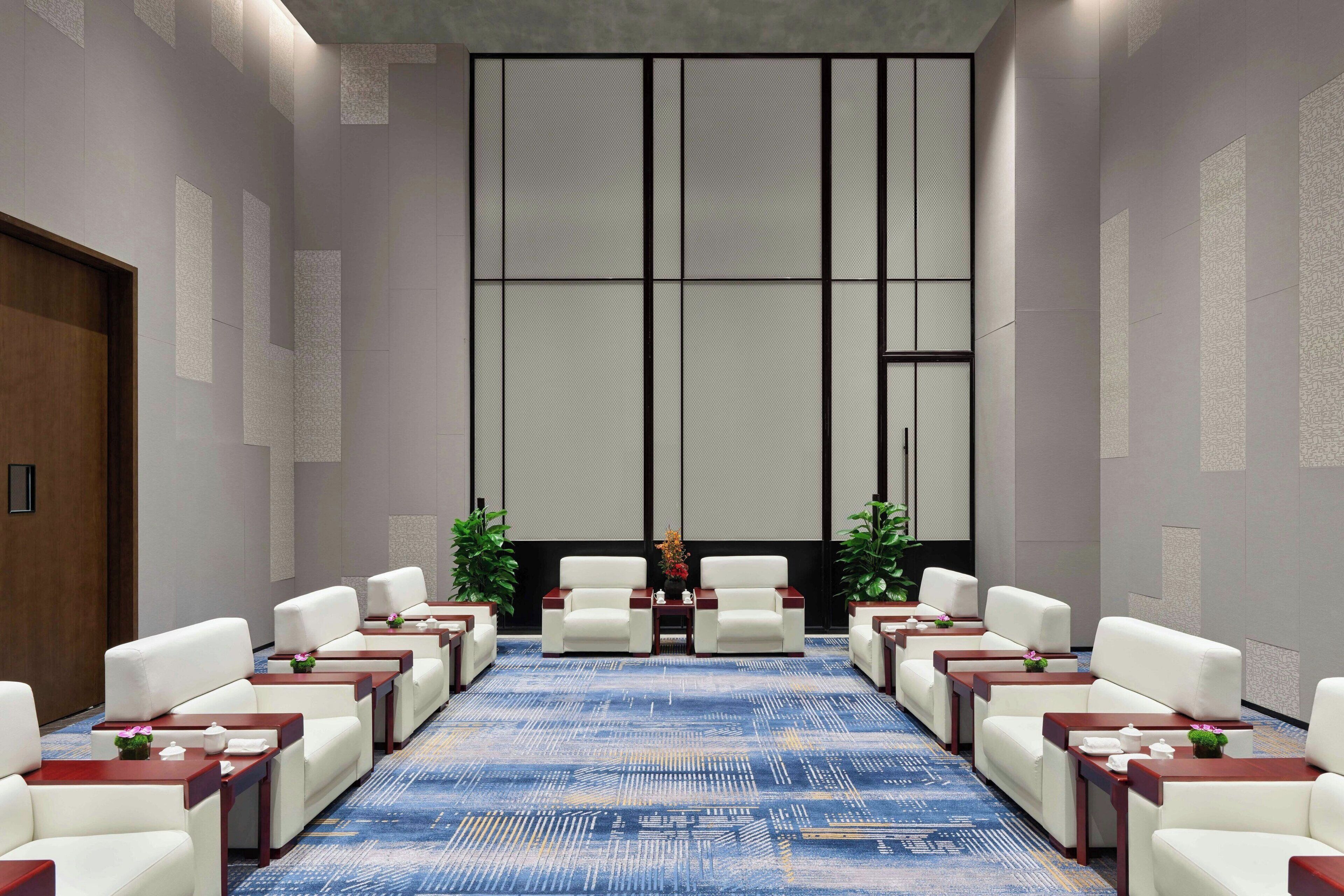 Un salón de conferencias con una larga mesa, sillas blancas y pequeñas mesas con centros de flores.